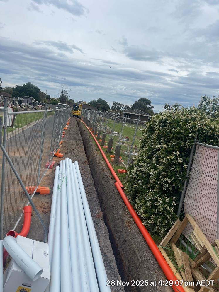 A long deep trench at a construction site with pipes and temporary fencing sitting alongside it.