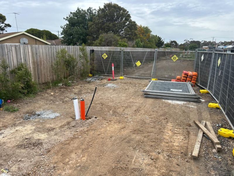 Two connecting pipes for a future toilet block stick out from the ground. The site is surrounded by temporary fencing. 