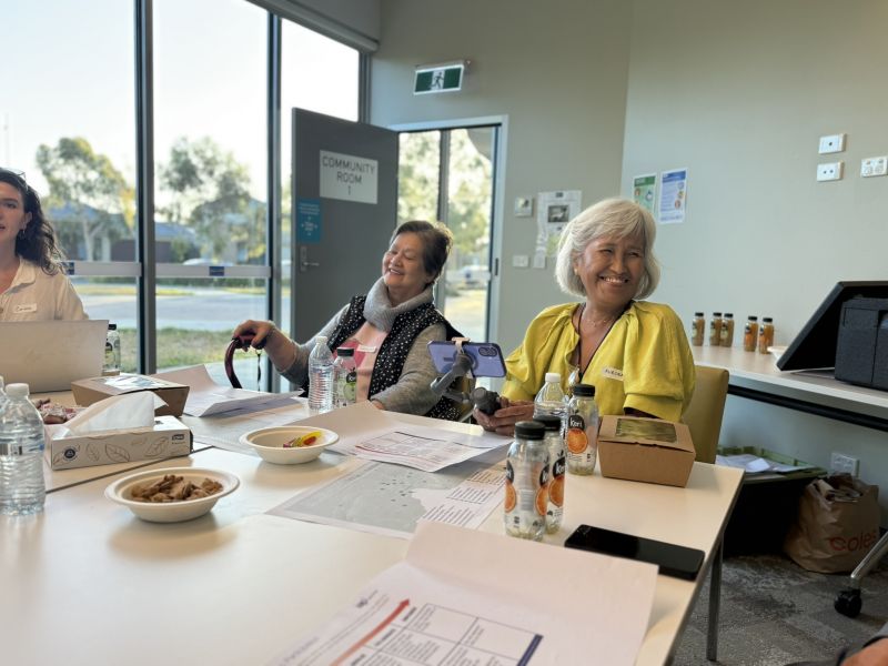 Two older women seated next to each other smiling at the people nearby.