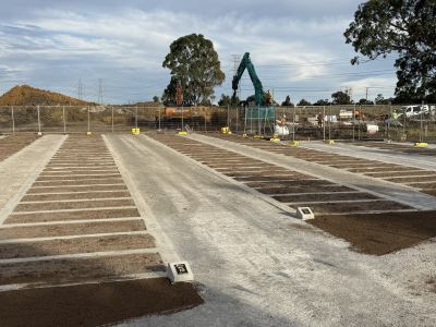 Rows of prepared monumental grave foundations. A digger and other construction vehicles are in the background.